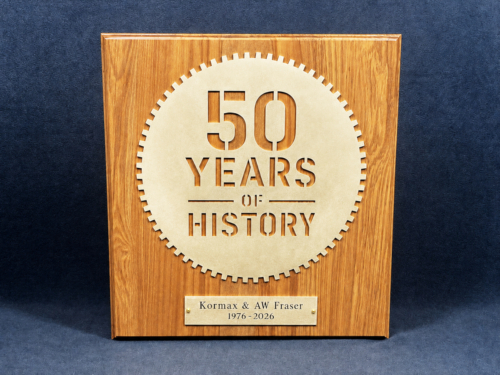 Photo of brass plaque on rimu board for 50 Years of History with AW Fraser and Kormax