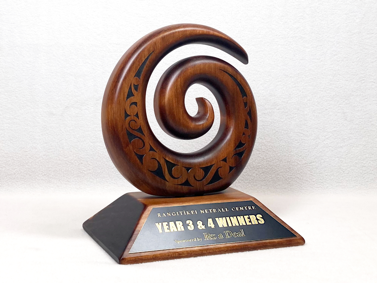 Wooden koru with an engraved black brass plaque